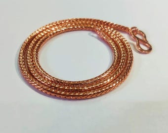May include: A coiled copper-colored chain necklace with a textured, woven design. The necklace is lying on a white surface and features a lobster clasp closure. The chain is a warm, reddish-brown color.