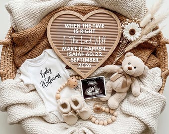 May include: A heart-shaped letter board with text, a white onesie with "Baby Williams", a teddy bear, baby shoes, and a sonogram image, all in a woven basket. The board reads "WHEN THE TIME IS RIGHT, I. The Lord Will MAKE IT HAPPEN. ISAIAH 60:22 SEPTEMBER 2026."