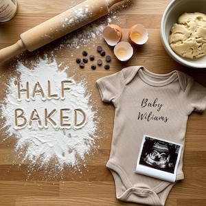 Puede incluir: Un body de bebé color beige con el texto "Baby Williams" y una imagen de ultrasonido, colocado sobre una superficie de madera con harina que deletrea "HALF BAKED". También hay chispas de chocolate, un rodillo y un cuenco con masa.