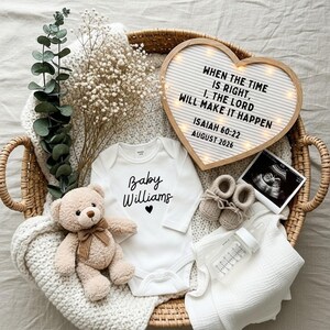 May include: A wicker basket holds baby items, including a white onesie with "Baby Williams" in script, a teddy bear, and a heart-shaped sign with text. Other items include baby shoes, a bottle, and a sonogram.