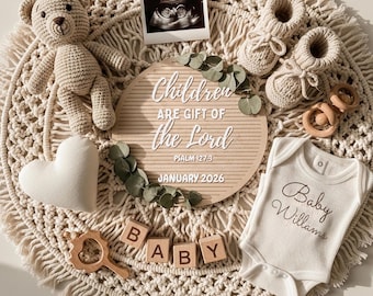 May include: A neutral-toned baby announcement arrangement featuring a crocheted teddy bear, heart-shaped pillow, baby booties, wooden blocks spelling "BABY", and a onesie with the name "Baby Williams". A letter board reads "Children are Gift of the Lord" and an ultrasound photo is included.