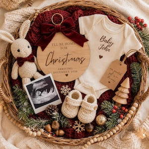 May include: A Christmas-themed baby announcement in a woven basket. Includes a wooden ornament with text, a baby onesie, ultrasound photo, crocheted booties, and a stuffed bunny. The ornament reads "I'll be home for Christmas, arriving December 2026."
