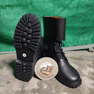 May include: Black leather combat boots with a lace-up design and a thick, textured sole. The boots have a tall shaft and a round patch with the text "INFINITY MILITARIA MILITARY BOOTS". The boots are size 9.