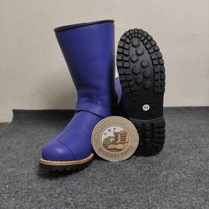 Może przedstawiać: Niebieskie skórzane buty z czarną podeszwą i brązowym wykończeniem. Buty mają pasek z klamrą i okrągłą naszywkę z napisem "INFINITY MILITARIA BOOTS". Podeszwa jest oznaczona numerem 11.