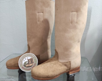 May include: A pair of tan leather knee-high boots with a suede toe and heel. The boots have a simple design with a single seam on the back of the shaft.