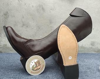 May include: Brown leather riding boots with a rounded toe and a high shaft. The sole is visible, showing a size 7. A circular sticker with text and a boot graphic is next to the boots. The boots are on a gray surface.