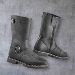Puede incluir: Un par de botas de moto de cuero negro. Las botas son de media caña, con hebillas y cremallera lateral. Las suelas son gruesas con costuras blancas. Botas diseñadas para protección y estilo.