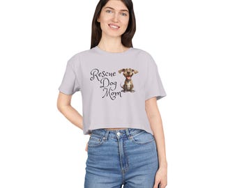 May include: A light gray crop top with the text "Rescue Dog Mom" in cursive script and a cartoon dog illustration. The dog is brown and white with a happy expression. The shirt is made of a soft material.