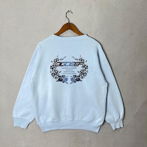 May include: Pale blue sweatshirt featuring the text "BIGDEEP" in a stylized font, encircled by a floral wreath design. The sweatshirt also displays the text "LONGBOARDERS HAWAII NORTHSHORE STYLE & WAVES". It is suspended from a wooden hanger.