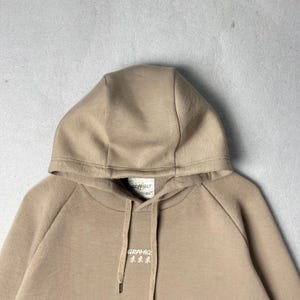 May include: A tan hoodie with a drawstring and a hood. The hoodie has the brand name "GRAMICCI" printed in white on the front. The hoodie is made of a soft, comfortable material.