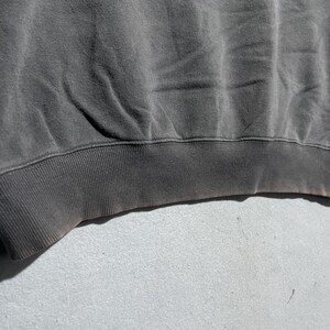 Puede incluir: Primer plano de una sudadera gris oscuro. El dobladillo inferior y los pu&ntilde;os son acanalados. La tela tiene un aspecto desgastado con sutiles variaciones de color, lo que sugiere que ha sido lavada y usada.