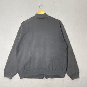 Puede incluir: Una sudadera con cremallera gris carb&oacute;n con cuello alto. La sudadera est&aacute; colgada de una percha de madera. La cremallera es plateada. La tela parece suave y desgastada.
