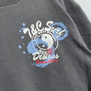 Puede incluir: Una sudadera gris con un dise&ntilde;o circular que muestra "T&C Surf Designs" y "Since 1971." El dise&ntilde;o incorpora un s&iacute;mbolo de yin-yang y "Hawaii Surf." El gr&aacute;fico es en blanco, azul y rojo.