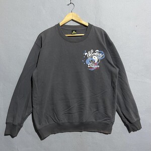 Puede incluir: Sudadera gris oscuro de cuello redondo con un gr&aacute;fico en la parte delantera. El gr&aacute;fico incluye el texto "Y&C Surf Designs" y un s&iacute;mbolo de yin-yang. La sudadera est&aacute; colgada en una percha de madera.