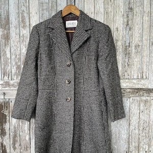 Peut inclure: Un manteau Sofia Rossi à motifs marron et noir, avec un col cranté, trois boutons et une coupe ajustée. Le manteau est suspendu à un cintre en bois sur un fond en bois vieilli.