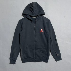 May include: A black zip-up hoodie with a hood and front pockets. A red logo is on the left chest. The hoodie has a full zipper and ribbed cuffs and hem. The hoodie is made of a soft, comfortable material.