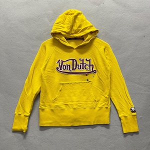 May include: Yellow hooded sweatshirt with the text "Von Dutch" in a purple and white design across the chest. The sweatshirt has a front pocket and a small skull and crossbones logo on the sleeve.