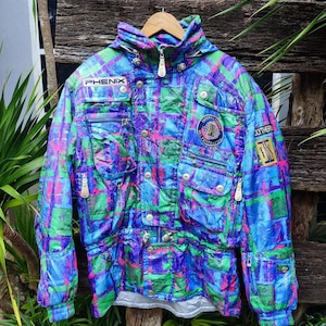 May include: A colorful vintage ski jacket with a plaid pattern in shades of blue, green, purple, and pink. The jacket features multiple pockets, zippers, and the brand name "PHENIX". It has a hood and a "OLYTHER" patch.