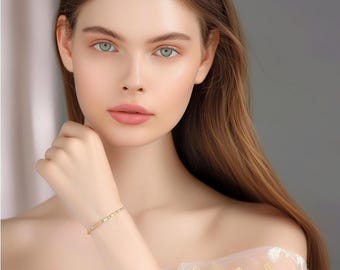 Peut inclure: Un fin bracelet en or avec un motif répété de petits accents scintillants. Le bracelet est porté au poignet, sur une peau claire. Le fond est un gris neutre et doux, pour une esthétique élégante et raffinée.