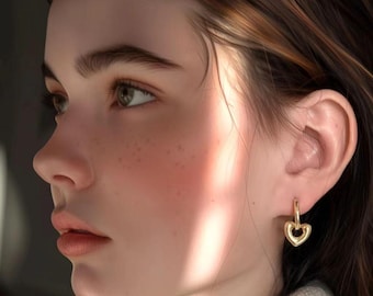Puede incluir: Perfil de una persona con piel clara, pecas y cabello castaño. La persona lleva pendientes dorados en forma de corazón. La iluminación es suave, con un brillo cálido en la cara.