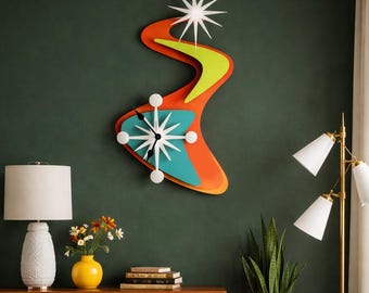 May include: A mid-century modern wall clock in a boomerang shape, featuring orange, teal, and yellow accents. The clock has white starburst hands and a white starburst at the top. The clock is mounted on a dark green wall.