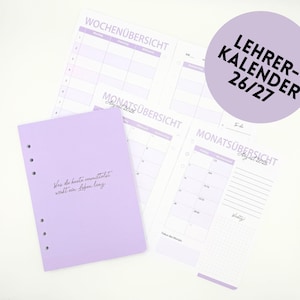 Könnte beinhalten: Ein hellvioletter Planer mit mehreren Kalenderseiten. Der Planer enthält Wochen- und Monatsansichten mit dem Text "LEHRER-KALENDER 26/27" in einem Kreis. Das Cover trägt den Text "Was du heute vermittelst wirkt ein Leben lang."