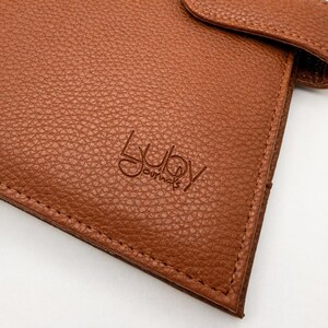 May include: Close-up of a brown leather journal cover with the embossed text "Lubu Journals". The cover has a textured surface and visible stitching along the edges. The journal appears to be new and unused.