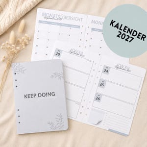 Könnte beinhalten: Ein hellgrauer Planer mit dem Text "KEEP DOING" und floralen Akzenten. Der Planer enthält Kalenderseiten für September 2027 und eine Kalenderseite mit dem Text "KALENDER 2027".