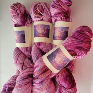 May include: Four skeins of pink and purple yarn with flecks of colour. Each skein has a label that reads "Cloud Fiber Co."
