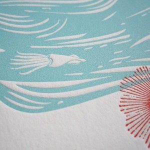 May include: A close-up of a teal blue and white print with a stylized squid and a red sun with a stylized face in the lower right corner.