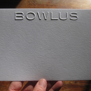 May include: A white card with the word "BOWLUS" embossed in white lettering.