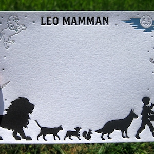 May include: A white card with a black silhouette of a lion, a cat, a dog, a squirrel, and a boy playing a musical instrument. The card has the text "LEO MAMMAN" printed in black at the top.
