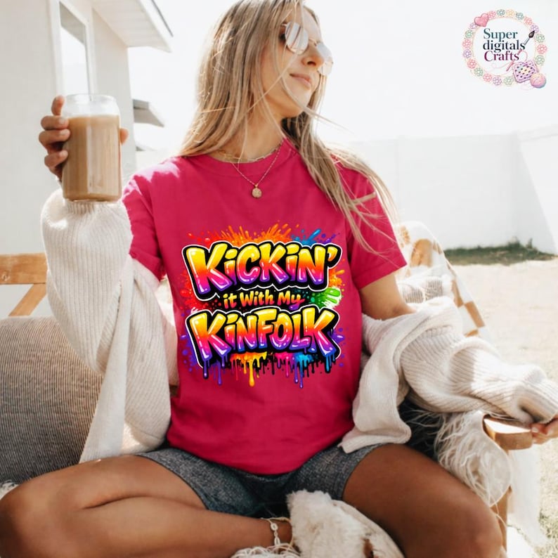May include: A magenta t-shirt with the text "Kickin' it With My Kinfolk" in a colorful graffiti-style design. The graphic features yellow, orange, blue, and green colors with dripping paint effects. The shirt is short-sleeved.
