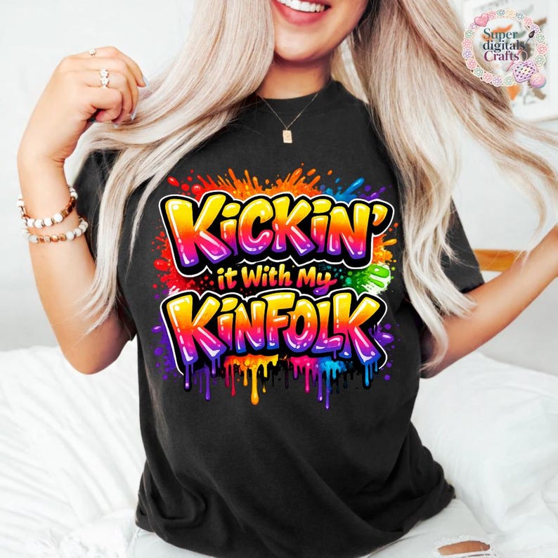 May include: Black t-shirt with the text "Kickin' it With My Kinfolk" in a colorful, graffiti-style design. The text is outlined in black and filled with vibrant colors, including yellow, orange, red, green, blue, and purple. The shirt has a crew neck.