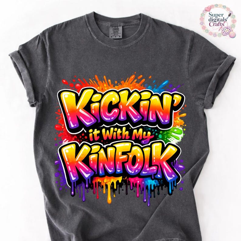May include: Dark gray t-shirt with the text "Kickin' it With My Kinfolk" in a colorful graffiti-style design. The text is outlined in white and features a vibrant mix of colors, including yellow, orange, red, purple, and blue.