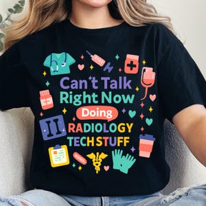 May include: Black t-shirt with a colorful graphic design. The design includes medical-themed icons and the text "Can't Talk Right Now Doing Radiology Tech Stuff". The design features a stethoscope, syringe, and other medical symbols.
