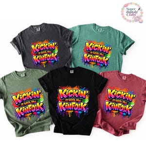 May include: Five short-sleeved t-shirts in various colors: black, dark gray, green, teal, and maroon. Each shirt features the text "Kickin' it with my Kinfolk" in a colorful, graffiti-style design.