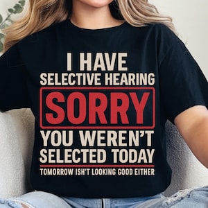 May include: Black t-shirt with the text "I HAVE SELECTIVE HEARING SORRY YOU WEREN'T SELECTED TODAY TOMORROW ISN'T LOOKING GOOD EITHER" in white and red lettering. The shirt is a casual wear item.