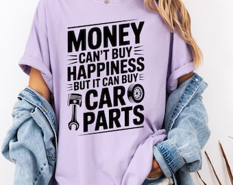May include: A light purple t-shirt with the text "MONEY CAN'T BUY HAPPINESS BUT IT CAN BUY CAR PARTS" in black. The design includes a piston and a tire. The person is wearing a denim jacket.
