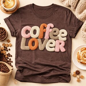 Könnte beinhalten: Ein braunes T-Shirt mit dem Schriftzug "coffee lover" in farbigen, strukturierten Buchstaben. Das Bild zeigt Kaffeebohnen, eine Kaffeetasse und Gebäck, was ein Kaffee-Thema suggeriert.