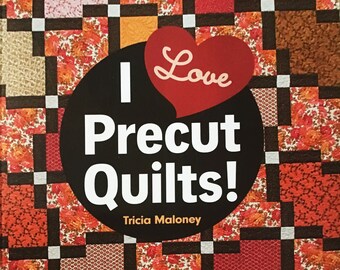 以下が含まれることがあります： 赤いハートと「I Love Precut Quilts!」というテキストが書かれた本の表紙。本のタイトルは「I Love Precut Quilts!」で、著者はトリシア・マロニー。副題は「16 Fast, Fun Projects」。本の表紙には、赤、オレンジ、茶色、白の布の正方形を使ったパッチワークのキルトのデザインが描かれている。「Use Jelly Rolls, Charm Squares, Layer Cakes, Fat Quarters & More」というテキストが表紙の下部に書かれている。