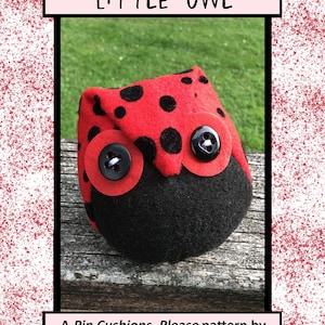 May include: A red and black felt owl pincushion with black polka dots and black button eyes. The pincushion is sitting on a wooden surface. "A Pin Cushions, Please pattern by Tricia Maloney P101"