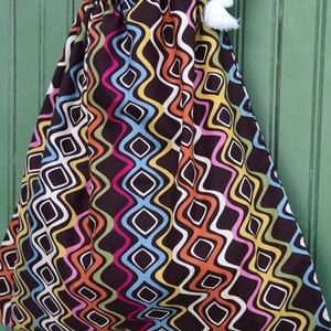 May include: A colorful drawstring bag with a wavy geometric pattern in shades of pink, orange, yellow, blue, green, and white on a brown background. The bag has white rope handles with tassels.