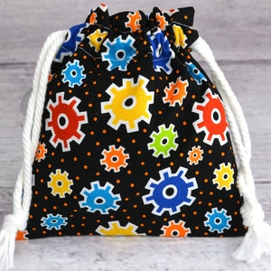 May include: A black drawstring bag with a colorful gear pattern. The bag has white drawstrings and is made of fabric.