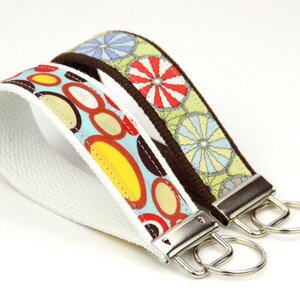 May include: Two colorful fabric keychains with metal key rings. One keychain has a blue background with orange, yellow, and brown circles. The other keychain has a green background with blue, yellow, and red flowers.