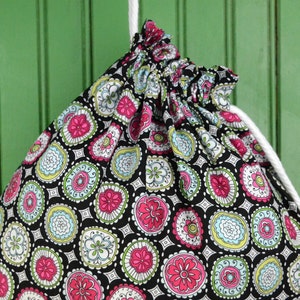 Puede incluir: Una bolsa de cordón negro con un cordón blanco y un estampado floral colorido. El estampado presenta flores rosas, verdes y azules sobre un fondo negro.