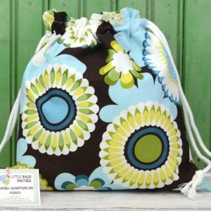 May include: A brown drawstring bag with a blue and green floral pattern. The bag has a white drawstring and is made of fabric. The bag is labeled "Little Birds Boutique" and "Drawstring Bag Medium".
