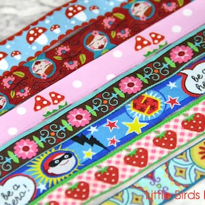 May include: Assortment of colorful patterned ribbon trims featuring various designs including mushrooms, flowers, stars, and strawberries. The ribbon trims are arranged in a stack and feature the text "be a hero!"