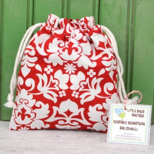 May include: Red and white reusable drawstring bag with a floral pattern. The bag is small and has a white drawstring. The bag is labeled "Little Birds Boutique Reusable Drawstring Bag (Small)".