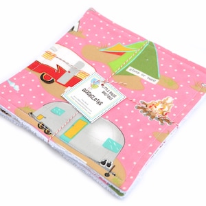 May include: A stack of pink and white washcloths with a camping theme. The washcloths feature a pattern of vintage campers, tents, and campfires. The text "glamp or bust!" is printed on the washcloths. The washcloths are tied together with twine and a tag that reads "Little Birds Boutique Washcloths".